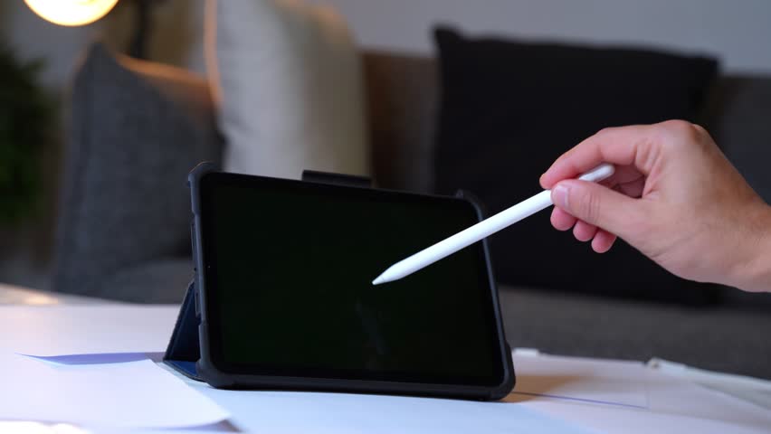 Tablet with green screen and stylus interaction in warm room. Ideal for app design, e-learning, creative content, and tech lifestyle mockups.