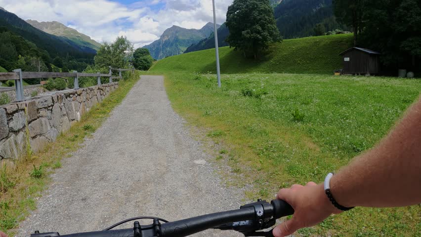 Experienced mountain cyclist pedaling along scenic alpine gravel road. Navigating winding path through verdant landscape with pristine mountain range backdrop