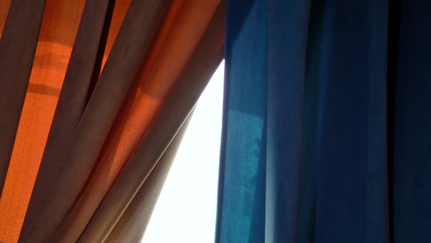 Warm sunlight filters through orange and blue velvet curtains. Ideal for interior, texture, mood, or cinematic storytelling visuals.