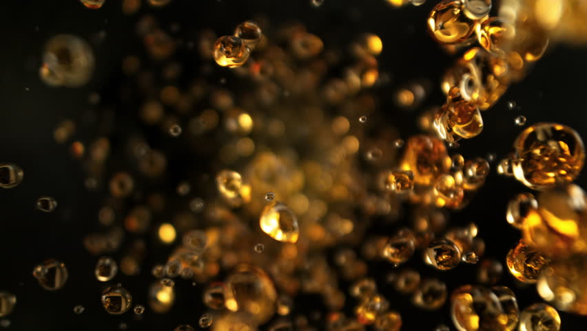Super Slow Motion Shot of Flying Golden Liquid Drops Towards Camera on Black Background at 1000fps.