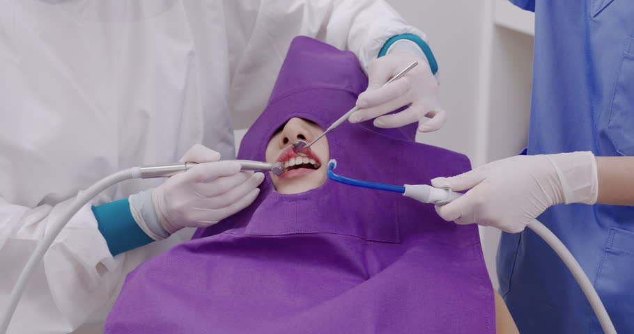 Dental procedure in progress as dentist uses curing light and suction with dental mirror to harden composite filling on asian female adult patient during treatment in clinic