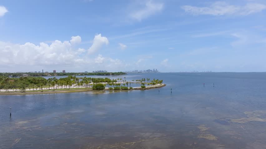 Aerial view of a serene coastline featuring palm trees, beach, and deep blue waters reflecting the clear sky, Coral Gables, Florida, United States.