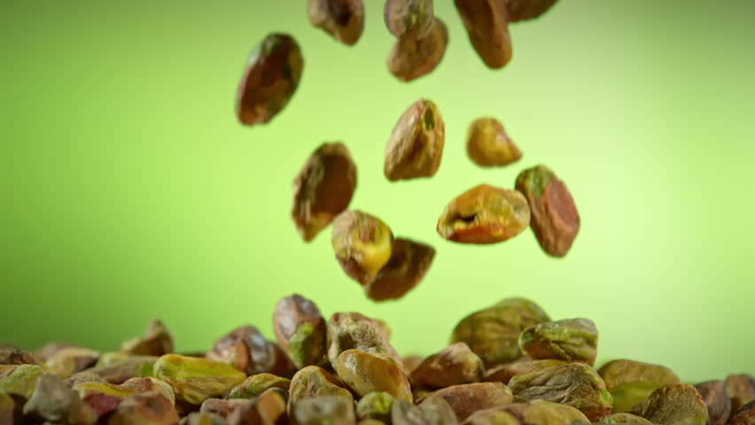 Super Slow Motion Shot of Falling Peeled Pistachio Nuts on Green Gradient Background at 1000fps.