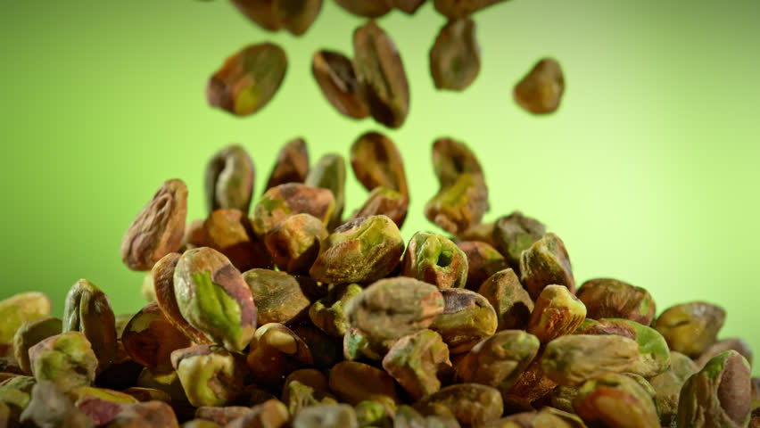 Super Slow Motion Shot of Falling Peeled Pistachio Nuts on Green Gradient Background at 1000fps.