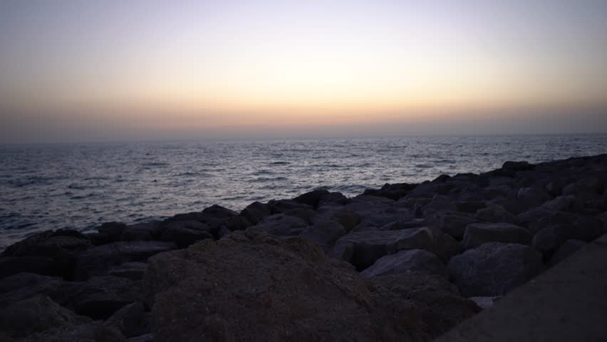 The calm beauty of the sunset casting warm shades over the ocean, when the waves carefully lower to the rocky coastline. This scene reflects the peaceful transition of nature into night.