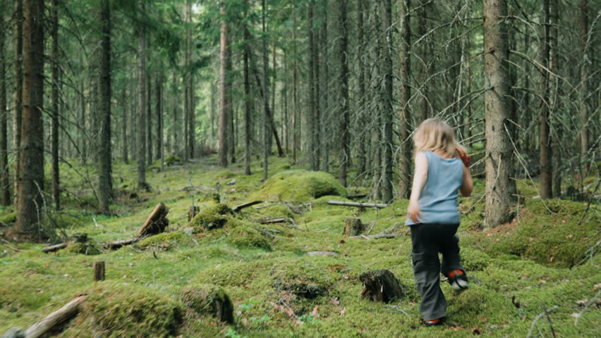 Free-spirited young kid runs over moss-covered woodland floor between trees
