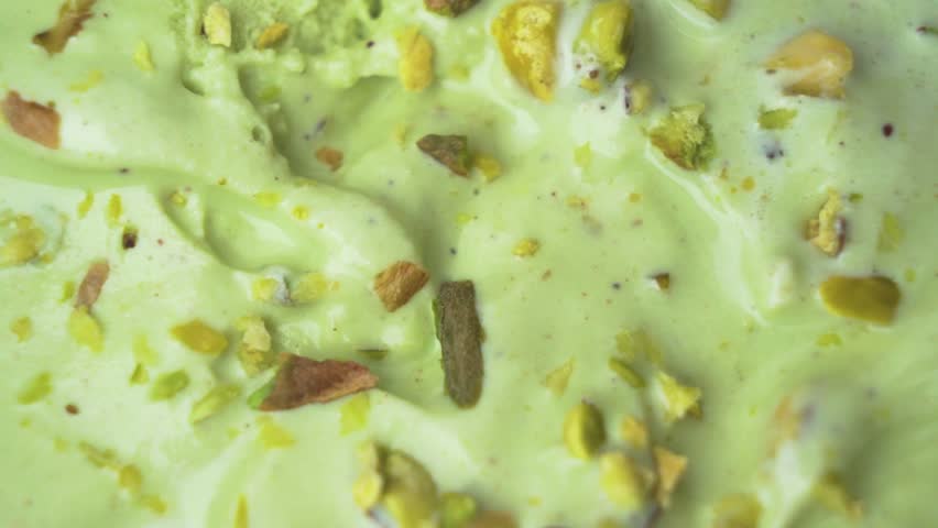 Close-up top-down shot of a creamy pistachio ice cream scoop with scattered raw nuts for texture.