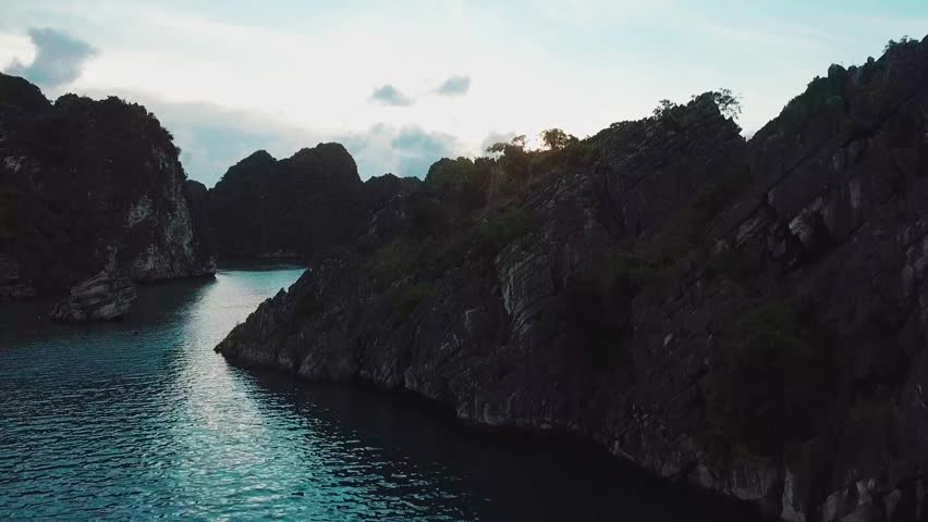 Aerial drone view of tranquil seascape with rocky islands scattered across calm ocean at twilight, soft light reflecting on water and silhouetted cliffs forming dramatic natural coastline.