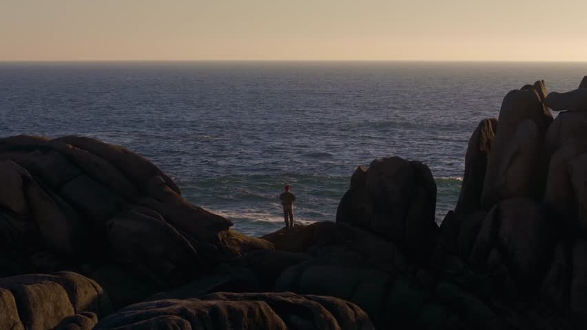 Person Standing On The Rock, Fishing In The Sea At Sunset. - wide shot