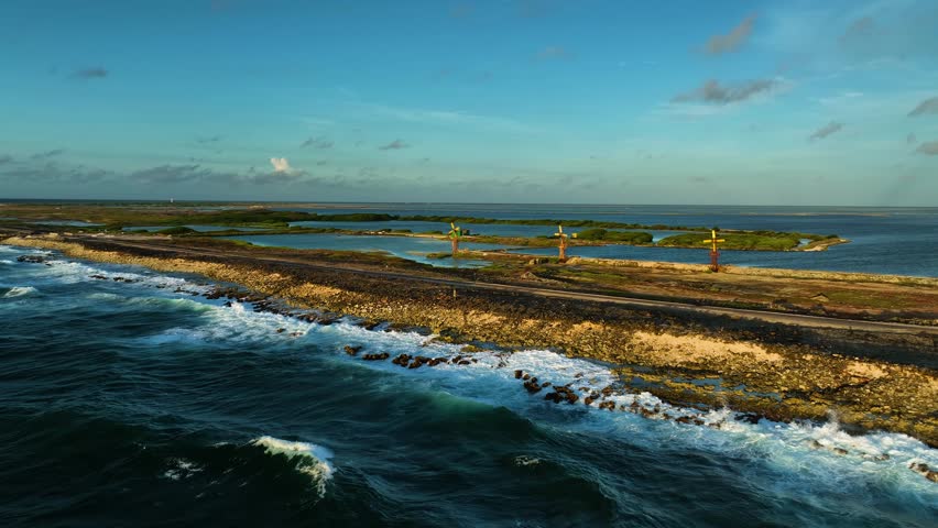 Aerial view of the rugged coastline, where turquoise waves crash against the shore near colorful windmills, Kralendijk, Bonaire, Caribbean Netherlands.