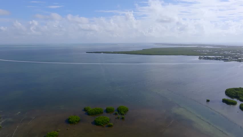 Aerial view of lush green mangrove islands on the water contrasting with the blue sky and the boat trail, Islamorada, Florida, United States.