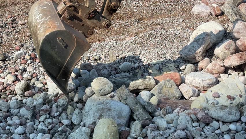Excavator bucket clearing large rocks from beach after storm. Coastal maintenance and cleanup work in seaside environment. High quality 4k footage