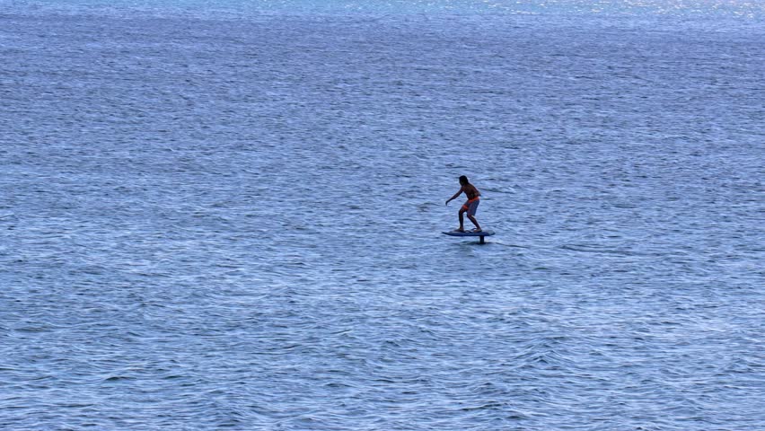 Thrilling hydrofoil boarding on calm blue ocean, athlete glides effortlessly over water, showcasing skill and balance