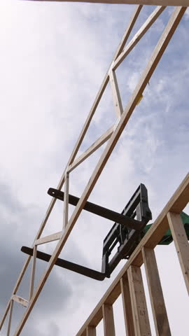Workers use telehandler lift to position wooden truss in building under construction as clouds gather above.