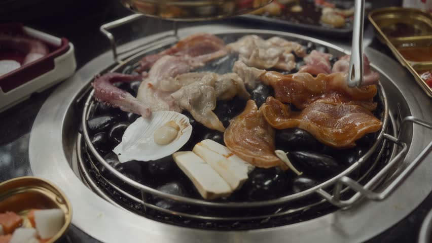 Hand cooking smoked grilled pork on iron grill pan in Korean BBQ in restaurant. Traditional Korea style food barbecue pork belly steak on charcoal grill.