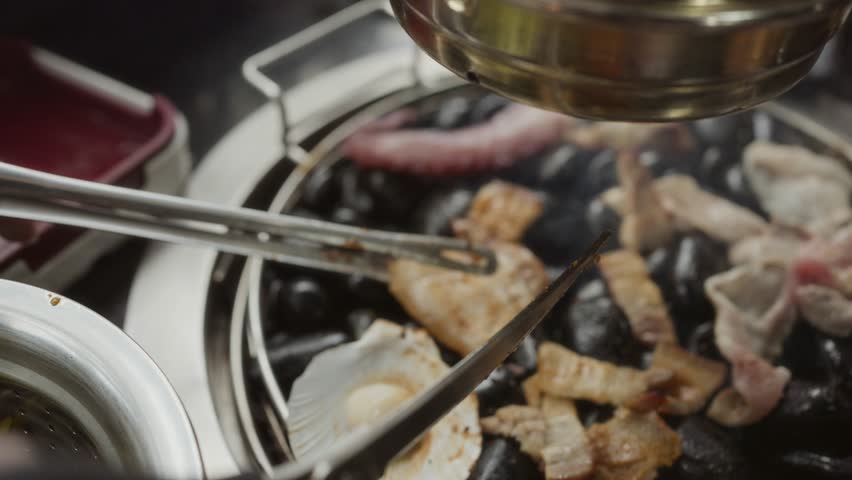 Hand cooking smoked grilled pork on iron grill pan in Korean BBQ in restaurant. Traditional Korea style food barbecue pork belly steak on charcoal grill.