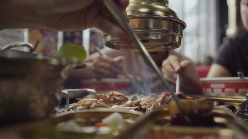 Hand cooking smoked grilled pork on iron grill pan in Korean BBQ in restaurant. Traditional Korea style food barbecue pork belly steak on charcoal grill.