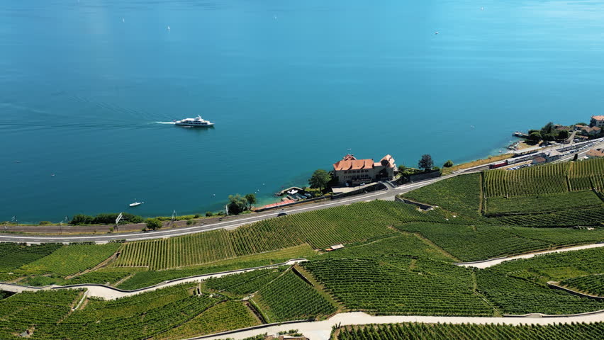 Aerial: white boat on Lake Geneva with Glerolles Castle and Lavaux terraced vineyards during the day in Saint-Saphorin, canton of Vaud, Switzerland, push in drone shot