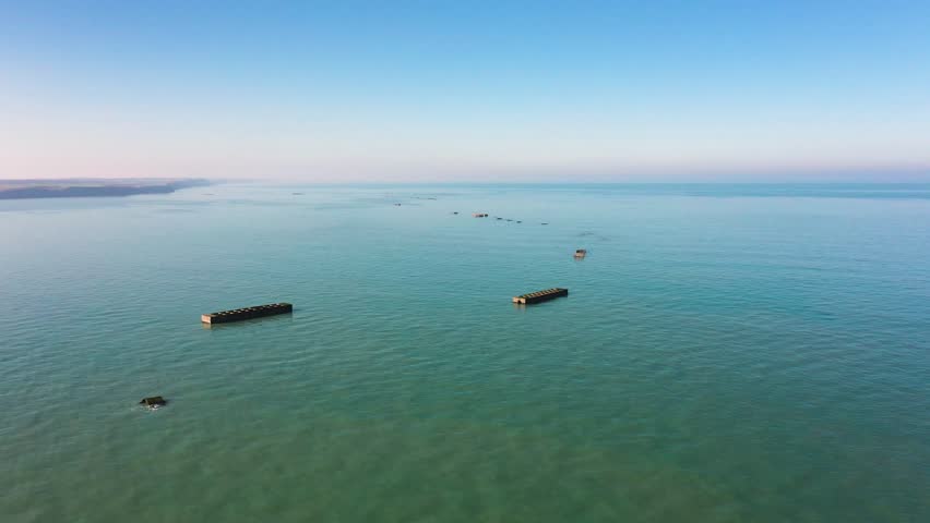 drone footage flying over Arromanches beach reveals the submerged and partially visible remains of the World War II temporary harbor.