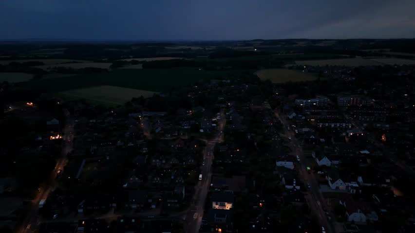 Night scene in charming small town of America. Dark blue sky after sunset. Lighting buildings and streets in the evening. Drone wide shot. Hills and farm fields in distance. Serene landscape in USA.