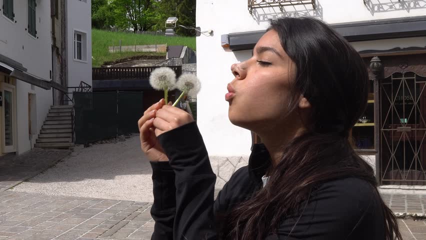 Young Woman Outdoor Blowing On Dandelions, Seeds Scattering In Sunlight. closeup shot, side view