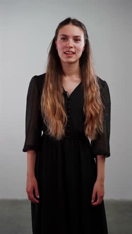 A young actress stands against a neutral background, delivering an expressive monologue without gestures to showcase her acting range for a demo reel