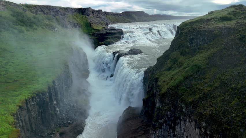 In this stunning display, a powerful Gullfoss waterfall tumbles down rugged cliffs in Iceland, surrounded by vibrant green vegetation. Gullfoss waterfall