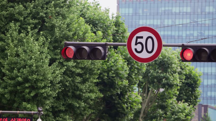 Slow motion view of Korean speed limit and traffic lights with trees and buildings in background