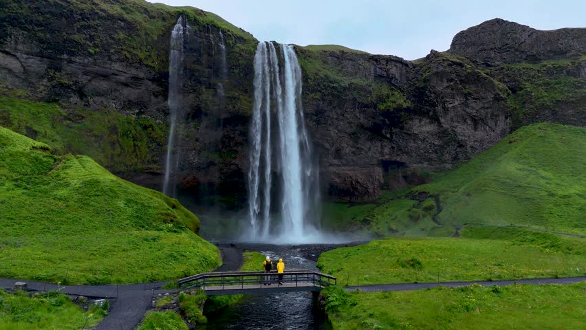 Witness a breathtaking Seljalandsfoss waterfall pouring over dramatic cliffs in Iceland, surrounded by vibrant greenery. Captured during a tranquil moment