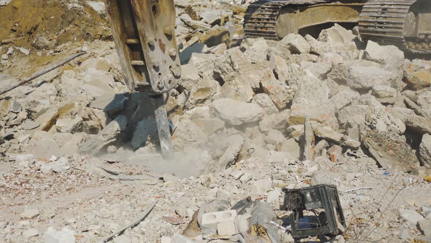 Construction excavator working with industrial jackhammer splits blocks of concrete, brick. Process of dismantling, demolished, destroyed house close-up. Hydraulic hammer of crushing machine.