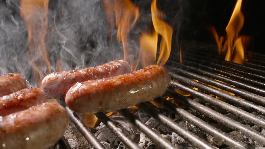 Juicy sausages sizzling on grill with smoke and flames in dark barbecue atmosphere