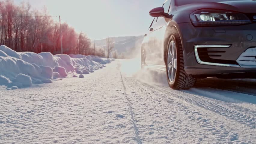Front wheel of a car spinning in snow due to poor traction while driving on a rural county road in winter conditions. Vehicle struggles to move through icy terrain.