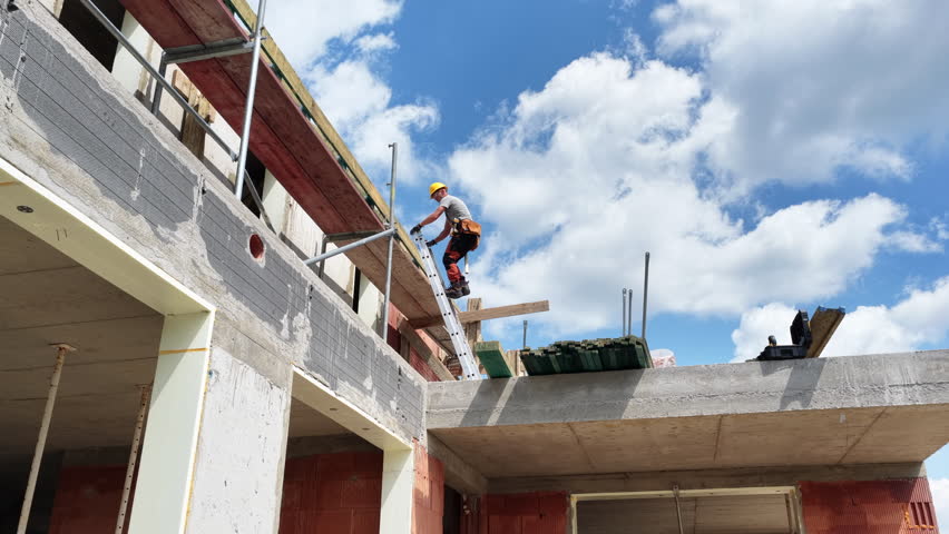 A construction worker climbs a ladder to reach the top of an incomplete building, working on the structure as clouds drift overhead, showcasing construction efforts.