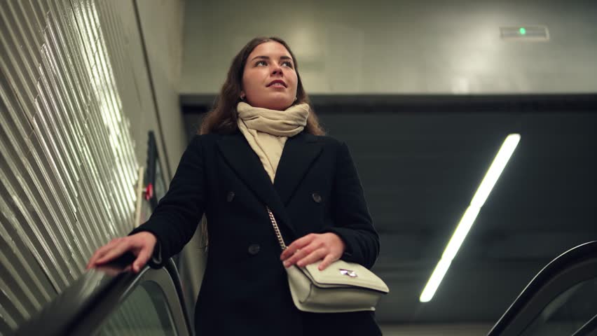 A determined young woman rides the escalator with confidence, looking ahead as she navigates through a busy transportation hub, embodying the spirit of modern commuting and the daily journey of