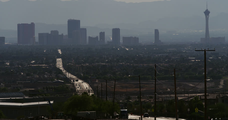 Desert cityscape silhouetted against a hazy skyline, with vacant lots strewn with trash and vast gleaming streets.