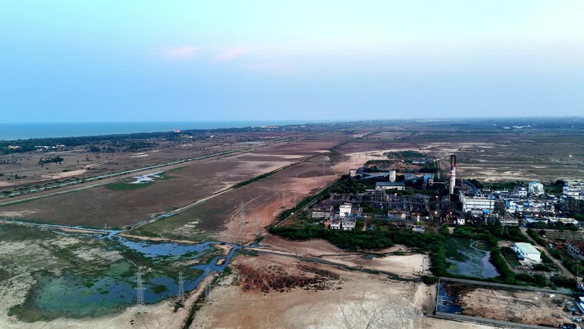 Aerial footage capturing an industrial facility in Tamil Nadu. The complex is surrounded by dry fields and water bodies, leading to the serene coastline on the horizon. Sidco Industrial Estate.