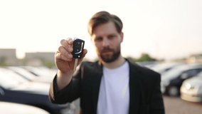 A businessman holds up a car key, smiling at the camera. He appears to be at a car dealership, with cars in the background. - Powered by Shutterstock - Get 15% off with code: PIKWIZARD15