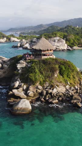 A beautiful coastal hut surrounded by cliffs and sea in Tayrona National Park. Aerial, Vertical Video