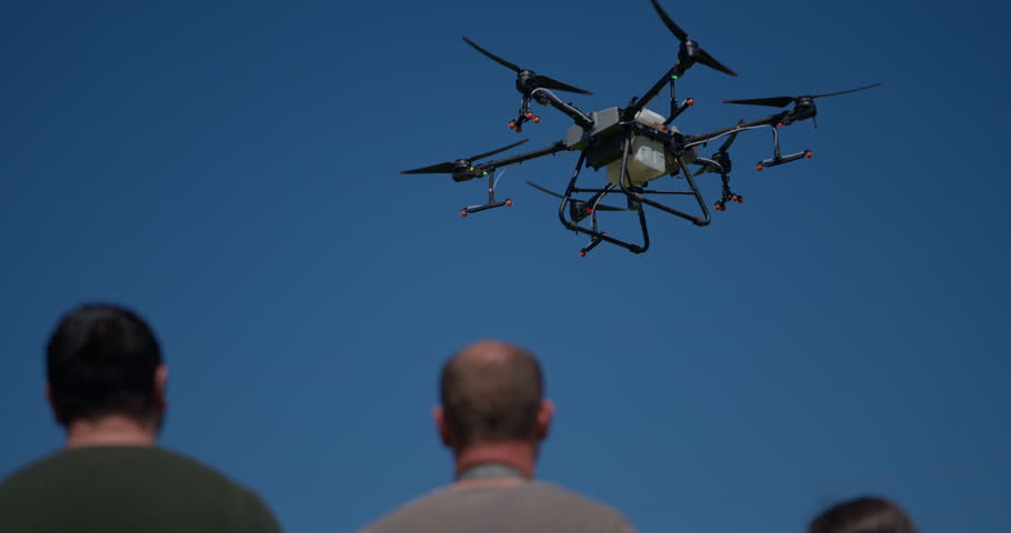 An innovative farmer operates a drone while standing in the middle of a field at sunset, using aerial technology to survey crops and monitor farmland as part of modern smart farming practices.