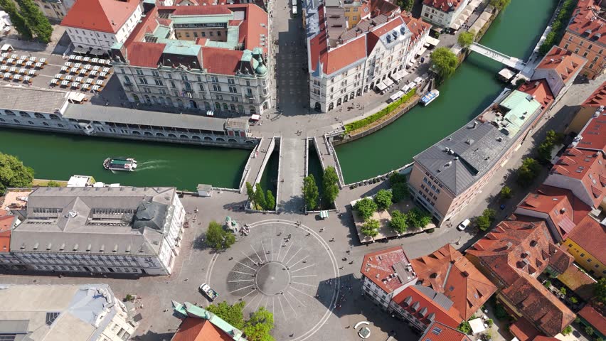 Aerial top down of Prešeren Square and Triple Bridge in Ljubljana’s Historic Center. Sunny day in summer season. Walking tourist and cruising boat.