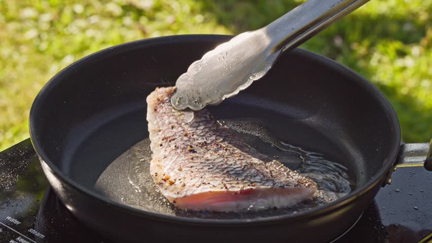 outdoor cooking. cook preparing fresh fish fillet on hot pan with oil for making delicious meal in garden, food closeup, outdoors natural light