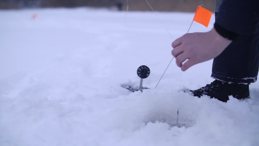 Fisherman pulling northern fish from ice fishing hole on frozen lake in winter using professional equipment. Excitement of ice fishing, winter adventure concept. Hobby of man outdoors on nature.