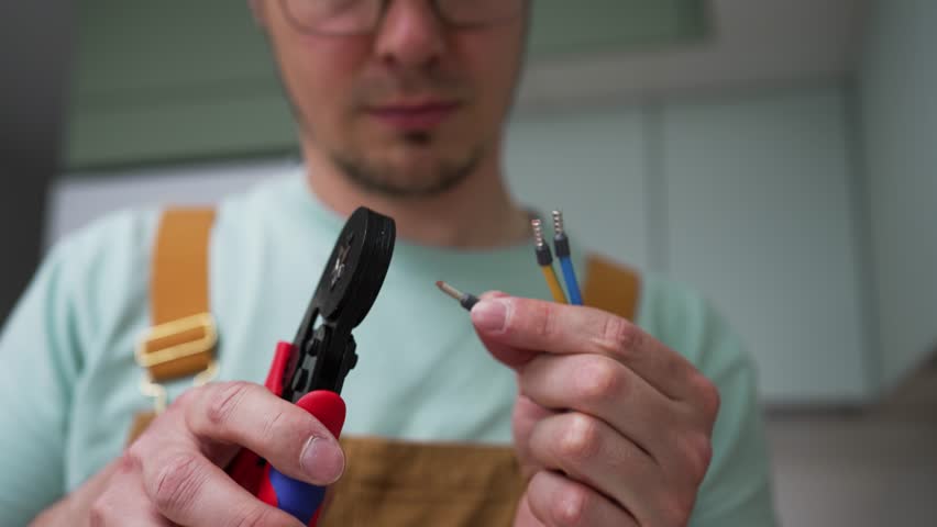 Professional electrician crimps small metal connectors onto electrical wires using crimping pliers, ensuring secure and reliable electrical connections