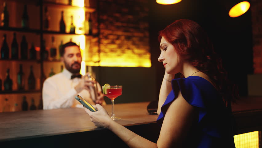 Lonely woman scrolling dating app on phone while sitting at bar counter