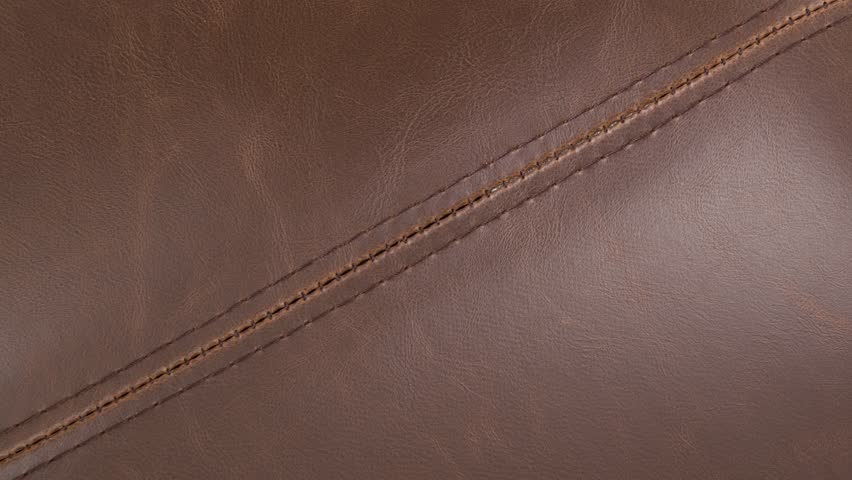 Camera zooms toward rich grain and precise stitching on dark leather