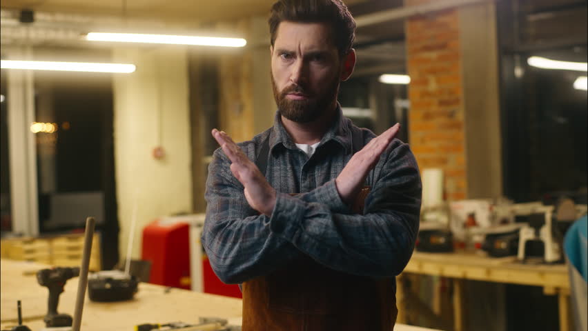 Serious Caucasian wood master man show prohibition gesture in workshop craftsman forbid builder joiner rejection guy demonstrating cross with hands male repairman ban no symbol artist decline refusing