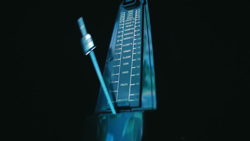 New, modern, shiny, black metronome, with a swinging pendulum, accurately beats in time, helping the musician not to lose the rhythm, on a black background. Closeup. Macro