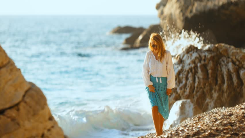 Woman enjoying a peaceful stroll along the rocky beach with gentle waves splashing in the background