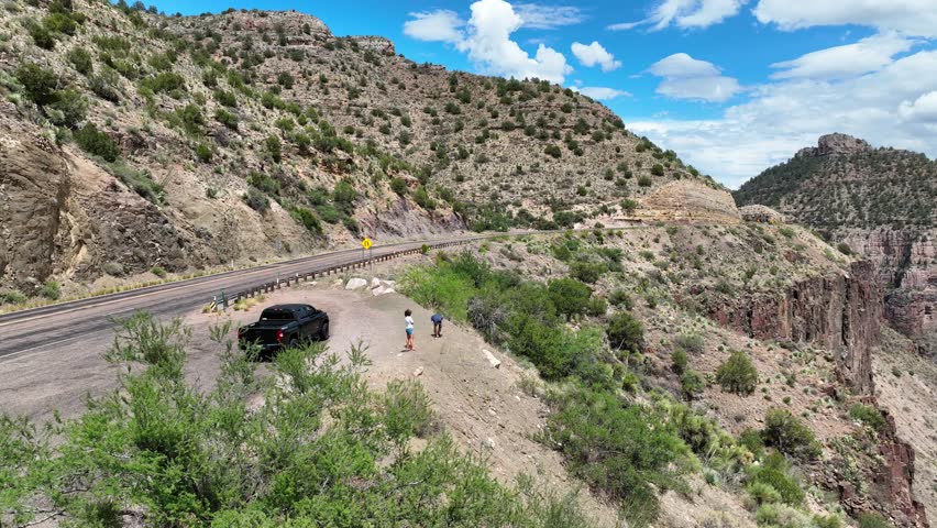 Aerial view of the arid Salt River Canyon, where a dark truck is parked by the roadside and two people gaze at the magnificent landscape, Salt River, AZ, United States.