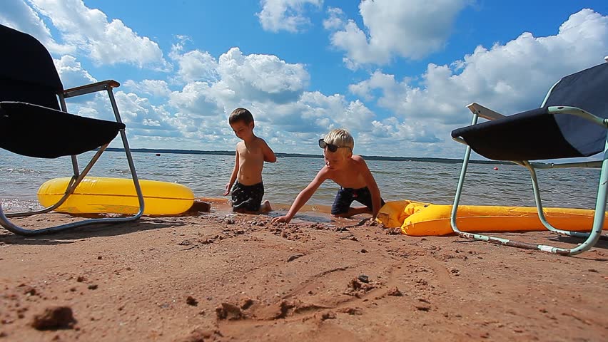 children digging in the sand on the beach in summer against the backdrop of a lake, clouds and blue sky reflected in the water